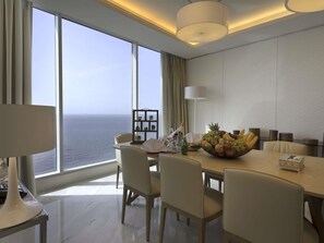 A modern hotel room with a large panoramic window, a dining table with chairs, a fruit bowl, and a lamp. - Novotel Jazan (Jizan)