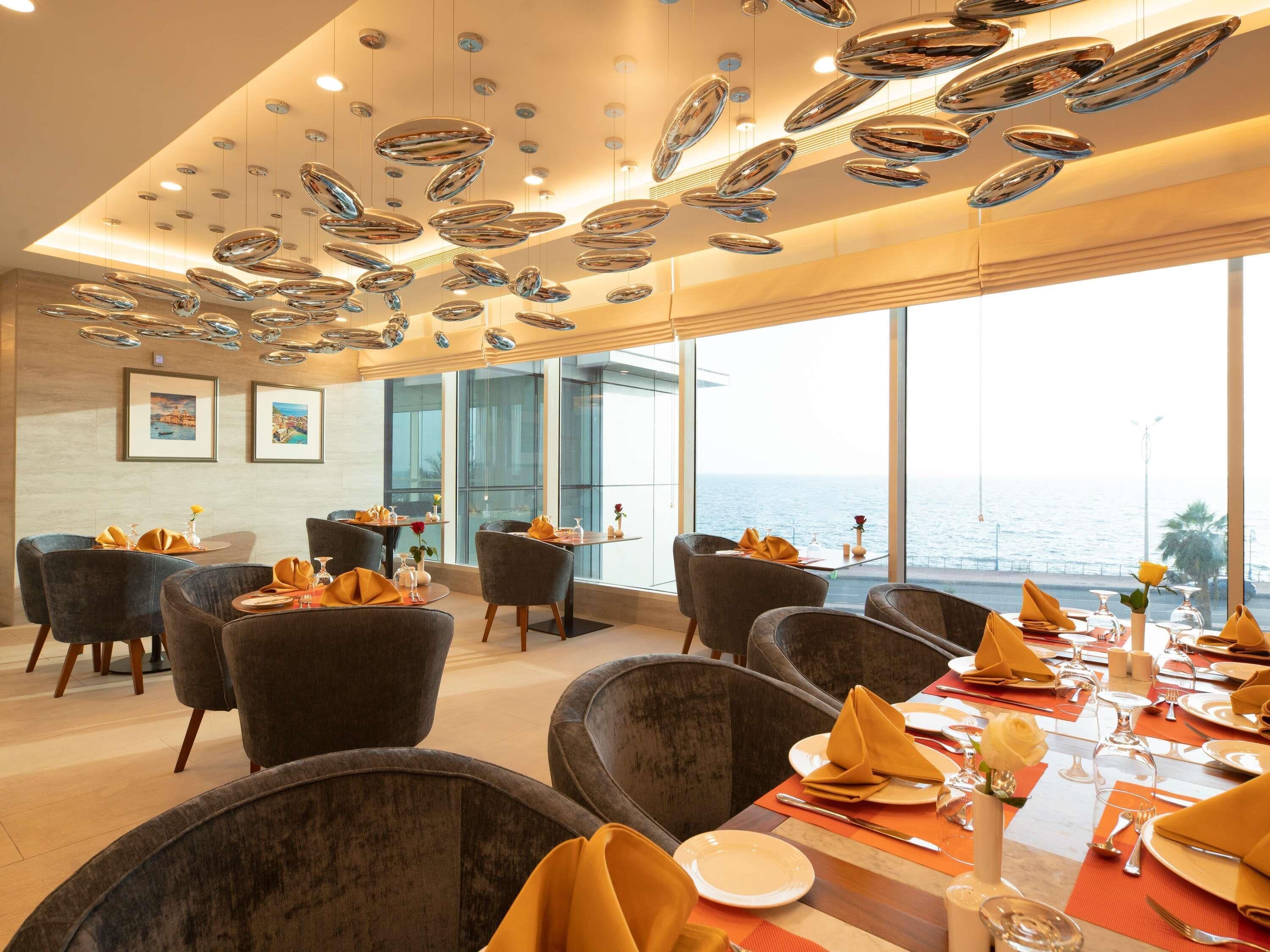 A dining area with tables set for service, chairs, and a view of the sea.