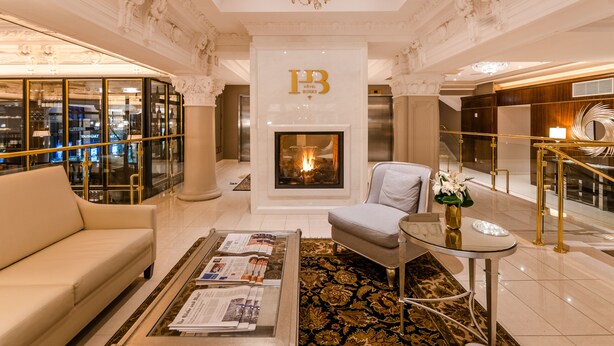 A luxurious hotel lobby with a fireplace, a sofa, a coffee table with magazines, and a chandelier.
