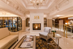 Eine luxuriöse Hotelhalle mit Kamin, einer Sitzecke, einem Couchtisch mit Zeitschriften und einer Kristallleuchtre.