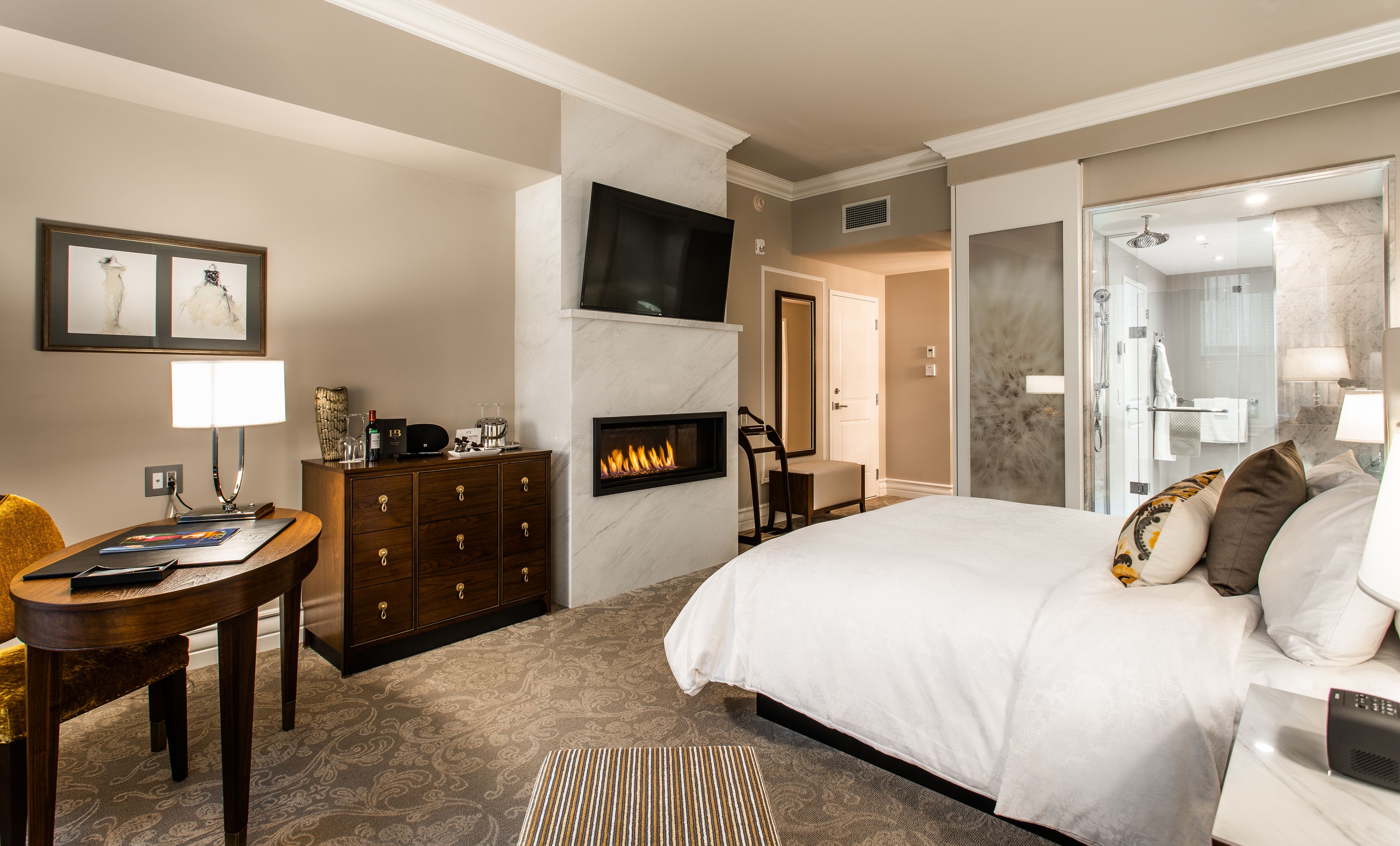 Une chambre d’hôtel avec un grand lit, une cheminée, un téléviseur fixé au mur, un bureau avec une lampe et une chaise.