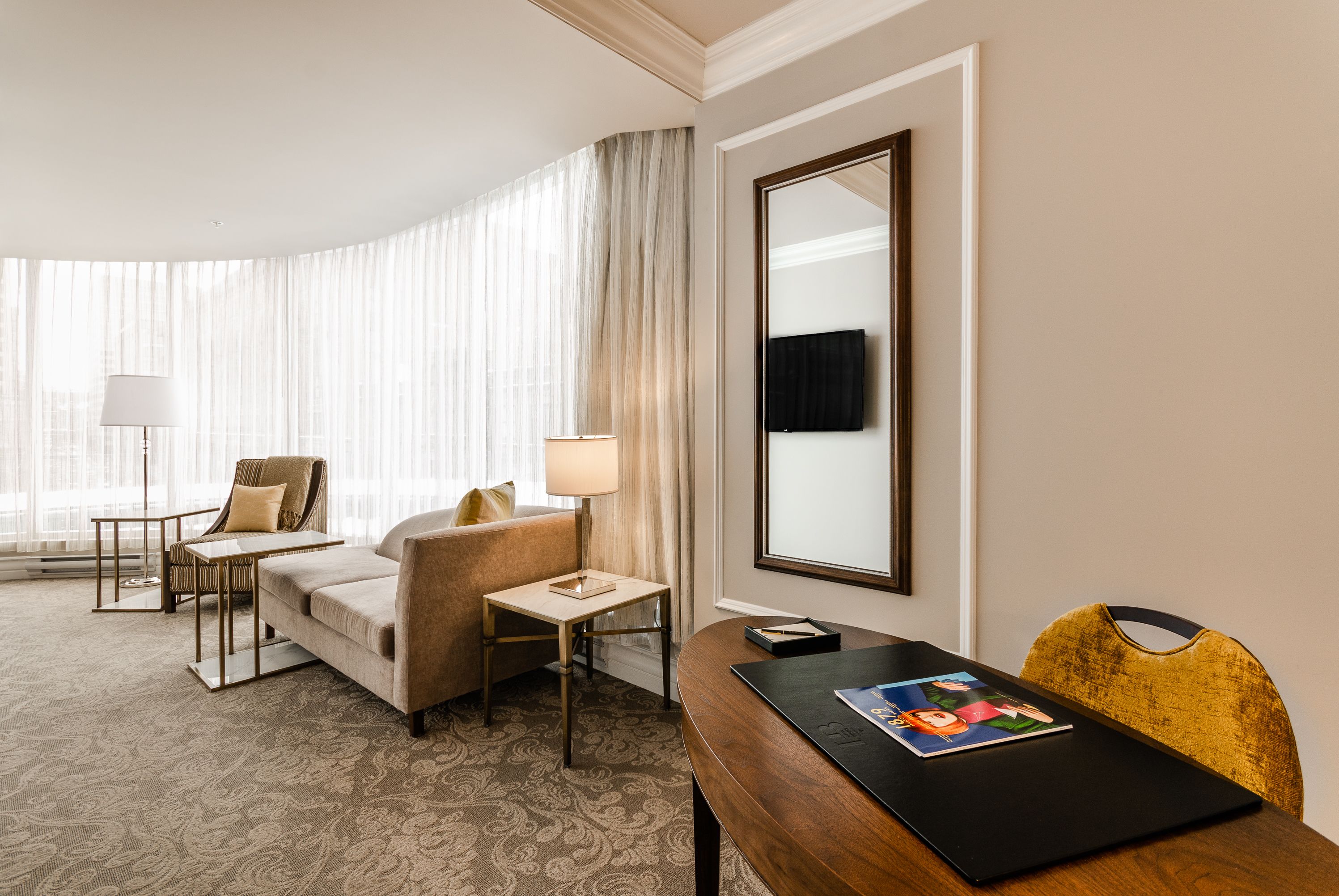 Hotelkamer met een bank, fauteuil, bijzettafeltje, lamp en een houten tafel met een tijdschrift.