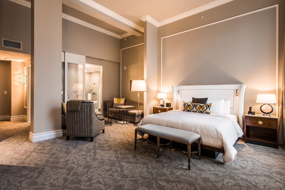 Ein Hotelzimmer mit einem großen Bett, einer Bank, einem Schreibtisch, einem Stuhl und einem Spiegel.