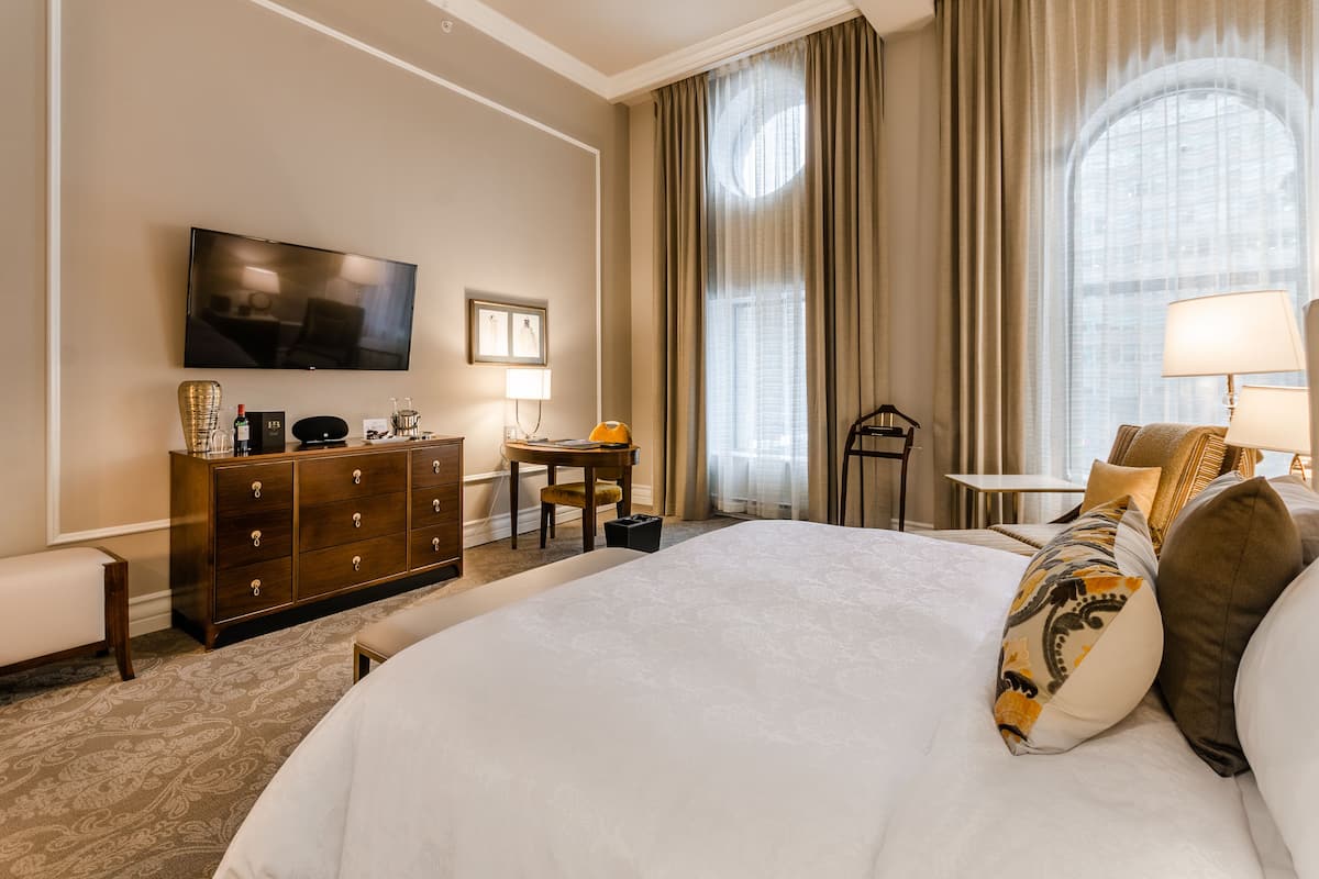 Ein Hotelzimmer mit einem großen Bett, einem Schminktisch, einem Fernseher, einem Schreibtisch mit Stuhl und einem Fenster mit Vorhängen.