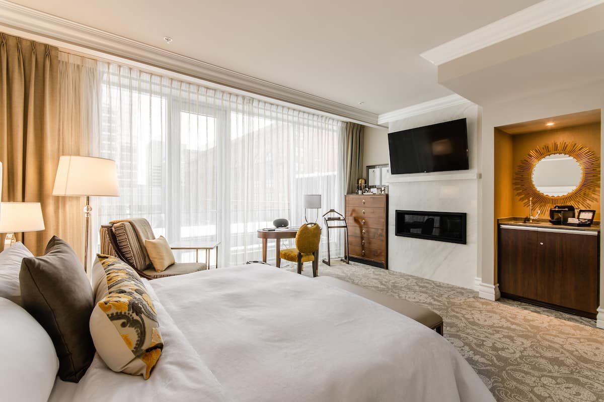 Ein Hotelzimmer mit einem großen Bett, einem Schreibtisch, einem Sessel, einem Fernseher, einem Spiegel und einem Kamin.