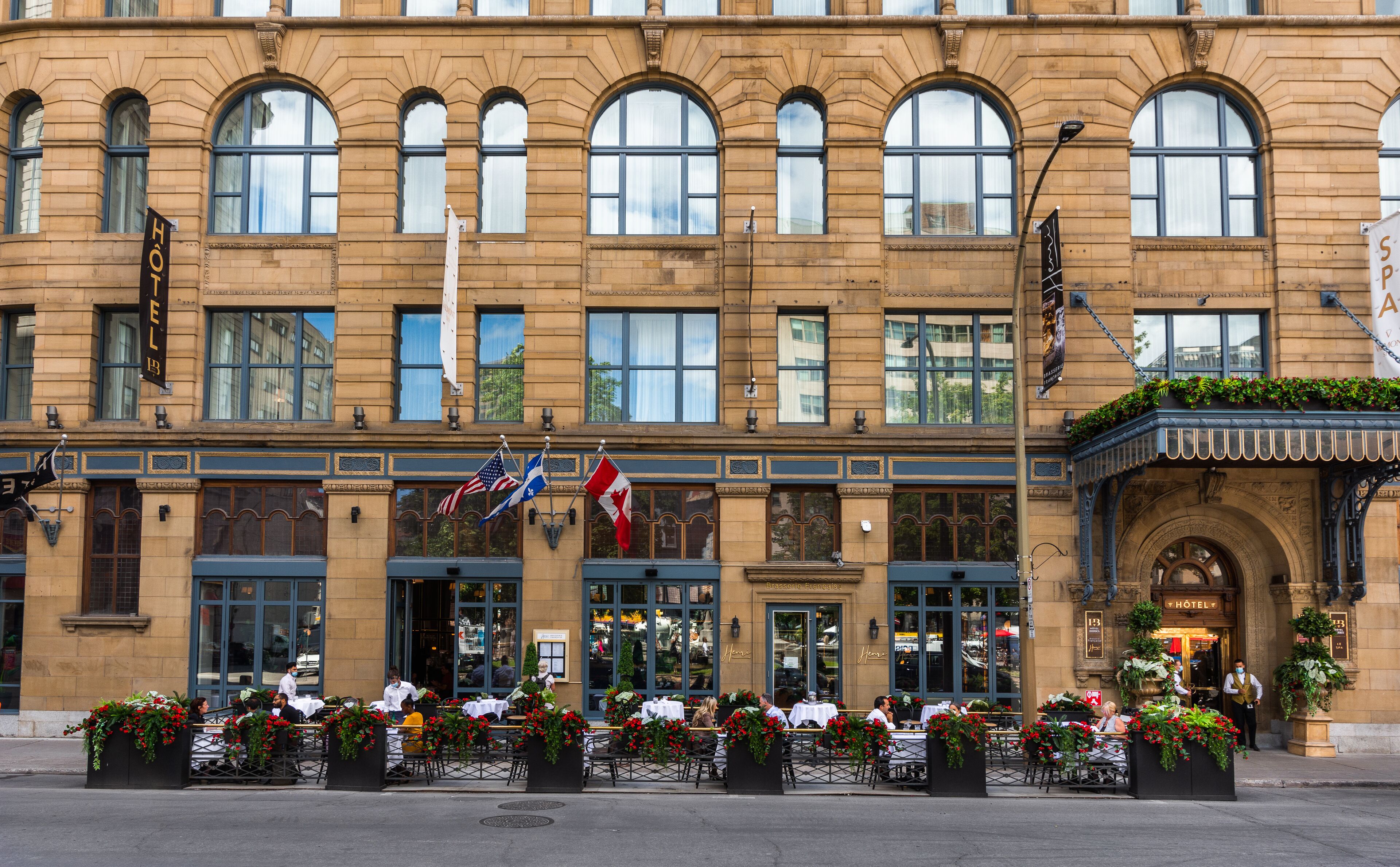 Un hôtel historique à la façade classique, doté de grandes fenêtres et d’une terrasse agrémentée de compositions florales.