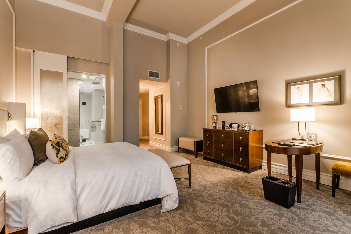 Ein Hotelzimmer mit einem großen Bett, einer Holzkommode, einem Fernseher und einem kleinen Tisch mit einer Lampe.