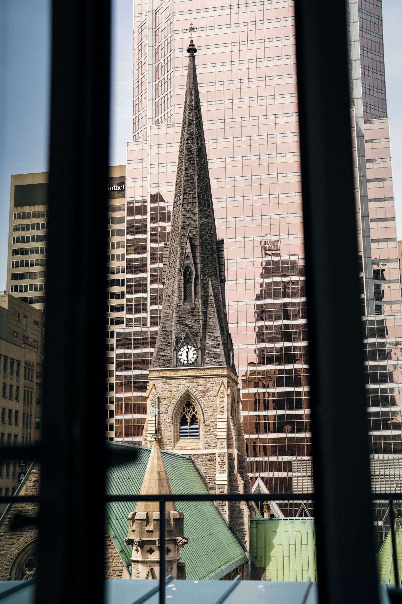 A church with a tall spire and a clock, surrounded by modern high-rise buildings.