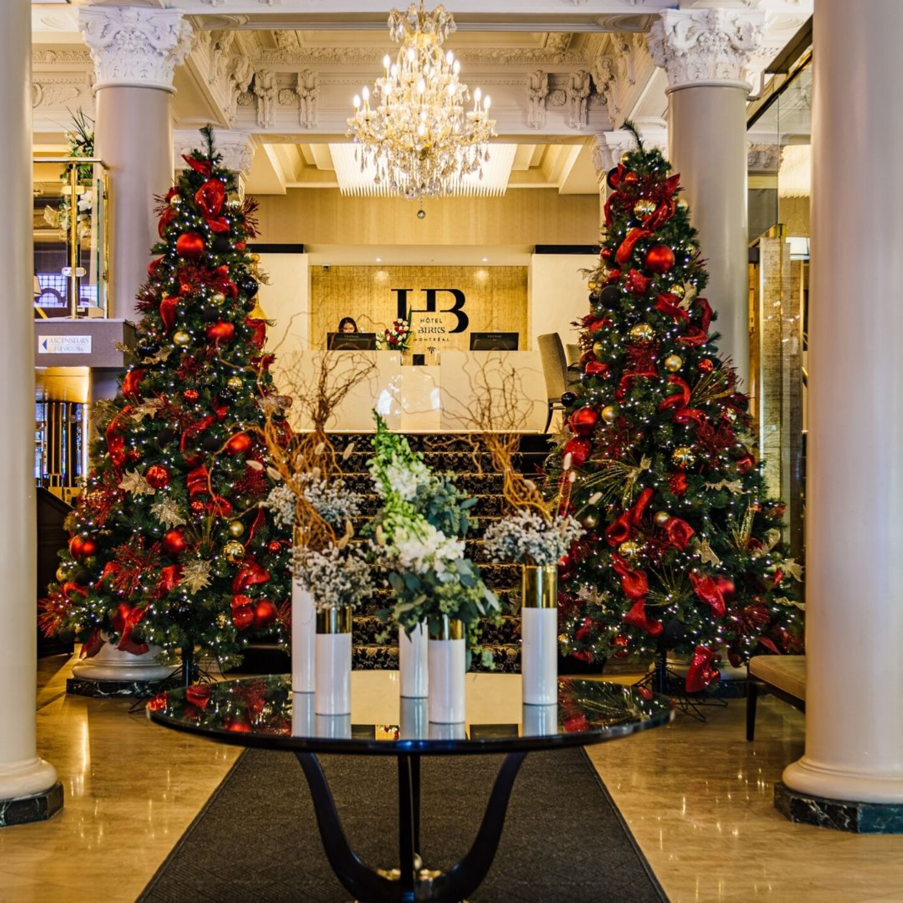 Un hall d’entrée avec deux sapins de Noël, un comptoir d’accueil et un lustre.