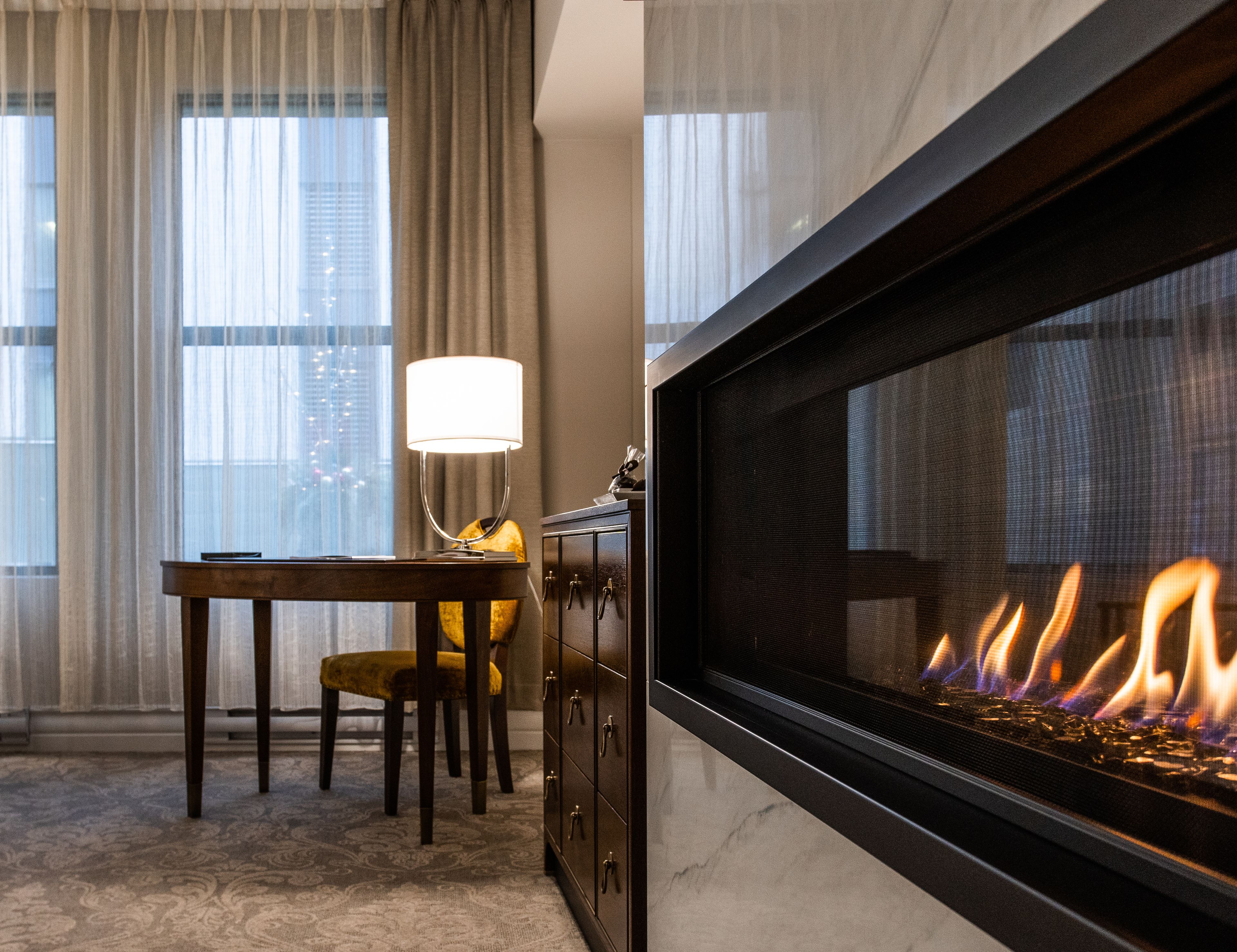 A modern living room with a fireplace, a dining area with a table and chairs, and large windows with curtains.