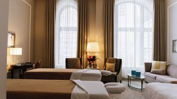 Une chambre d’hôtel avec deux lits, un coin salon comprenant un canapé et des fauteuils, une petite table et une lampe.