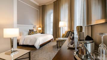 A hotel room with a bed, bedside tables, a desk, a chair, a minibar, and curtains.