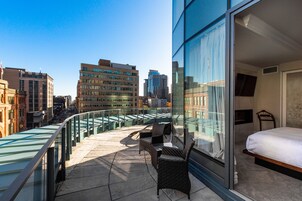 A balcony with a glass railing, a bed, and a chair.