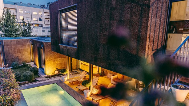 Un espace piscine extérieur moderne, doté de chaises longues et d’un jacuzzi, entouré d’un mur en pierre et agrémenté de plantes en pot.