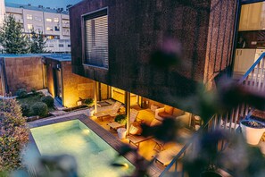 Un espace piscine extérieur moderne, doté de chaises longues et d’un jacuzzi, entouré d’un mur en pierre et agrémenté de plantes en pot.