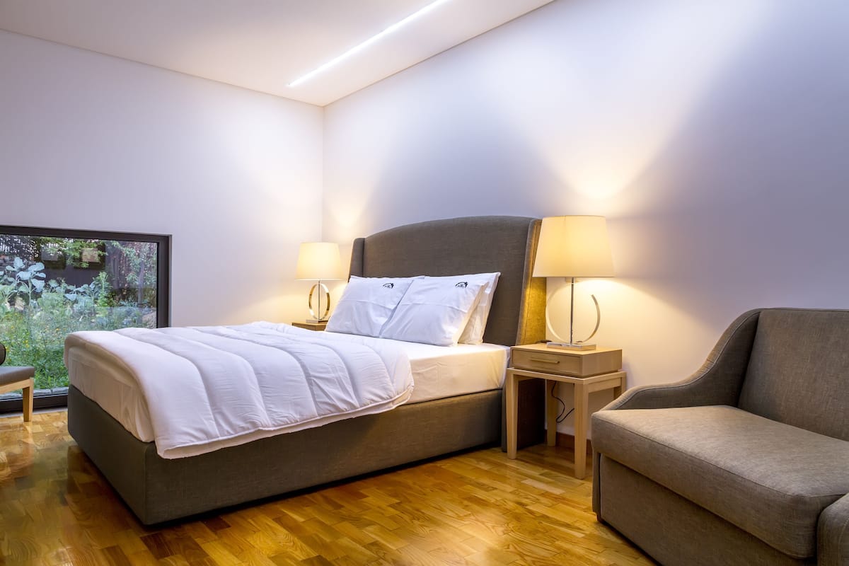 Una habitación de hotel moderna con cama, mesitas de noche, un sofá y vistas a zonas verdes.