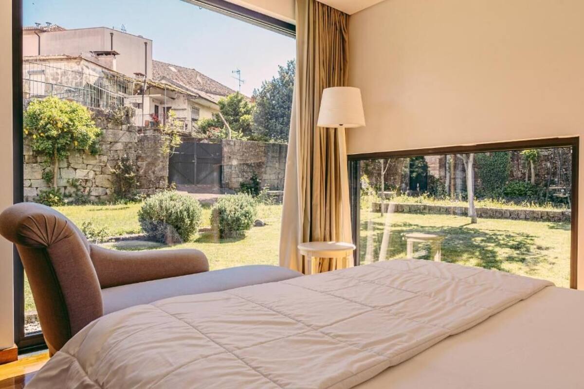 Un dormitorio con una cama grande, una silla, una lámpara y vistas a un jardín y edificios.