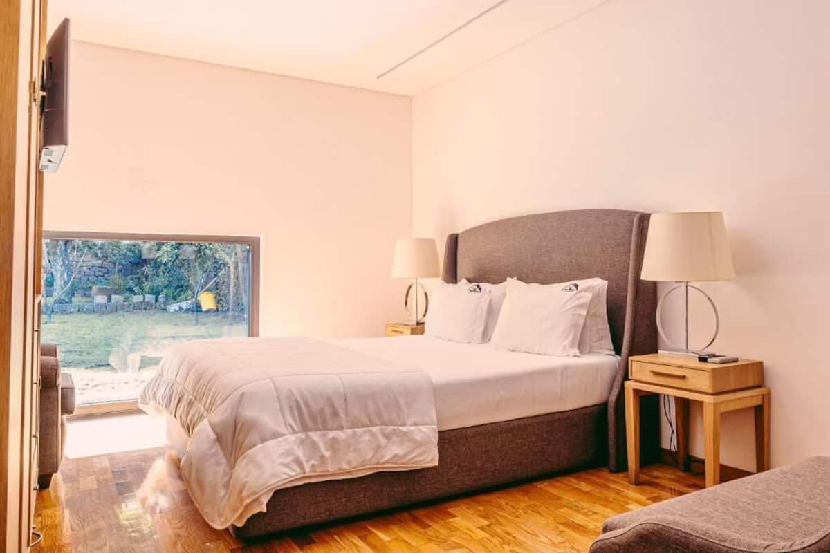Un dormitorio con cama, mesitas de noche, lámparas y vistas a un jardín.