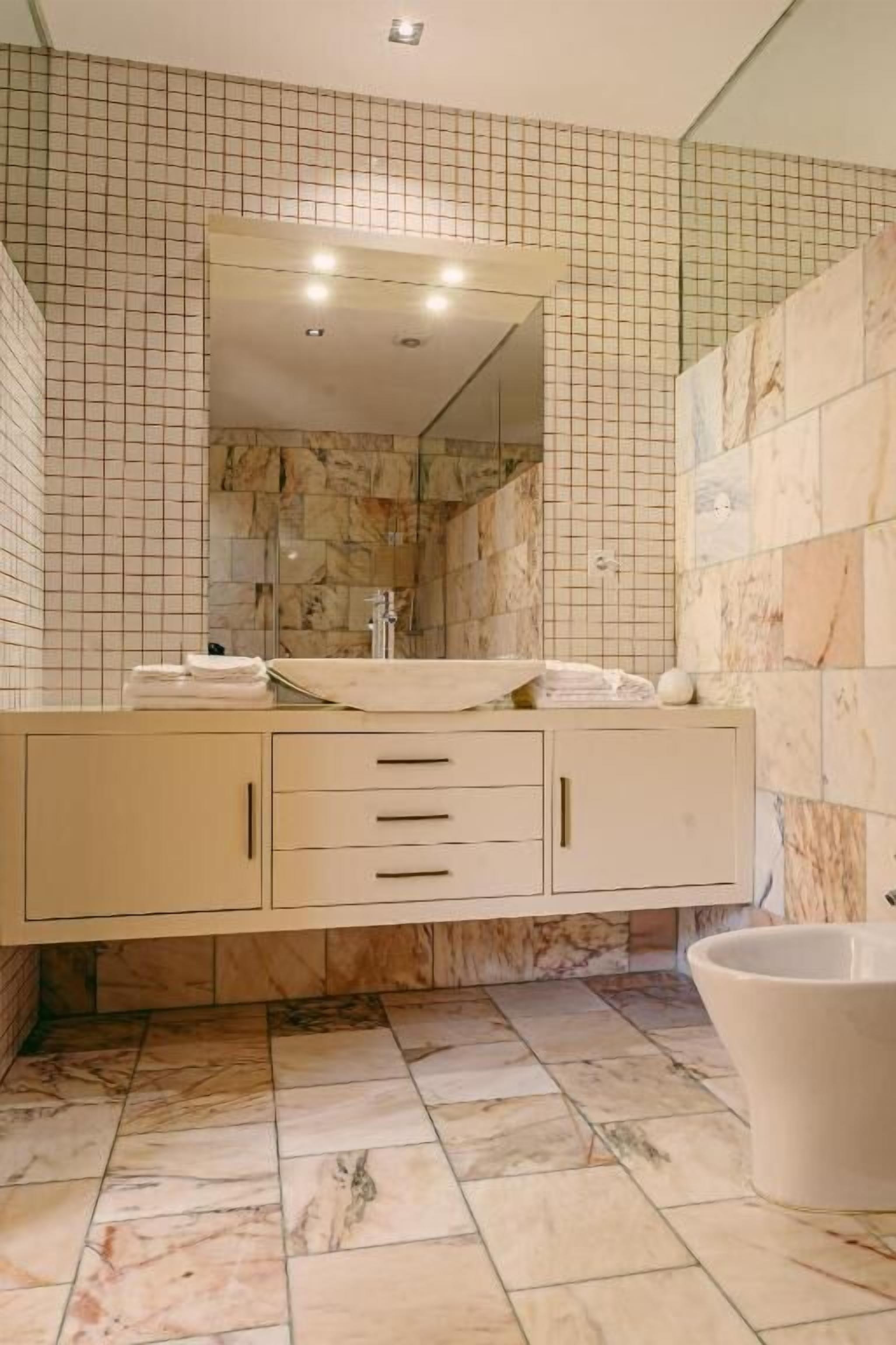 A bathroom with a marble-tiled floor, a large mirror, a sink with a marble countertop, and a white bathtub.