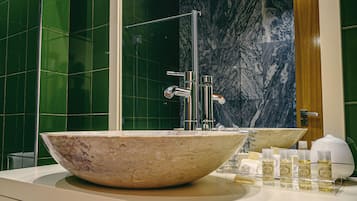 A bathroom with a large marble sink, green tiled walls, a shower, and a mirror.