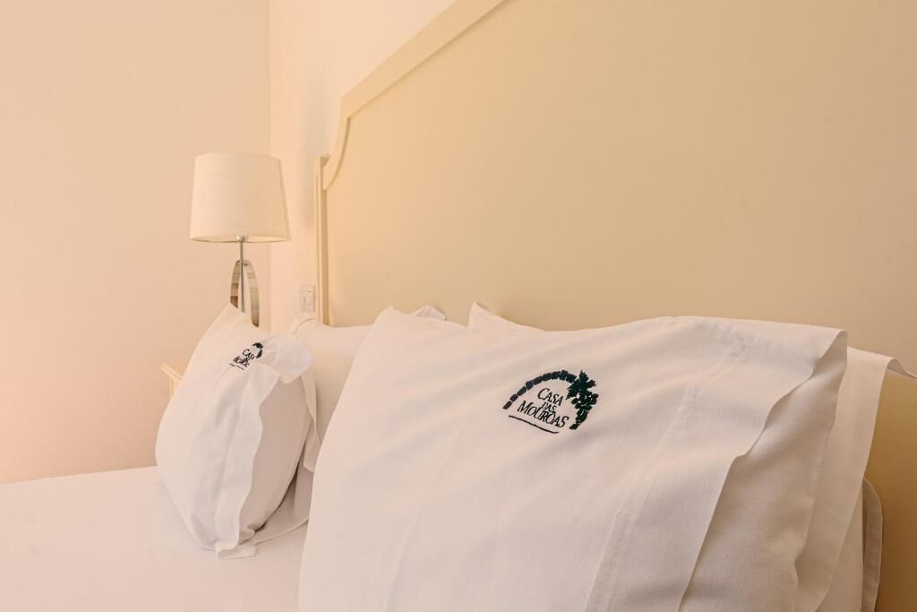 A hotel room with a bed, a lamp, and a pillow with a logo.