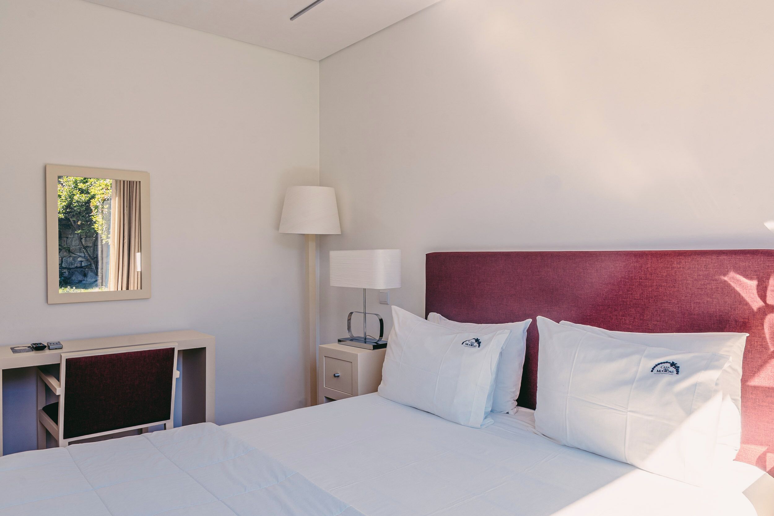 Una habitación de hotel con cama, escritorio, mesita de noche, lámpara y un cuadro en la pared.