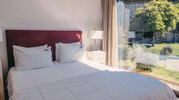 Habitación de hotel con una cama grande, una mesita de noche, una lámpara y vista a un patio con un árbol.