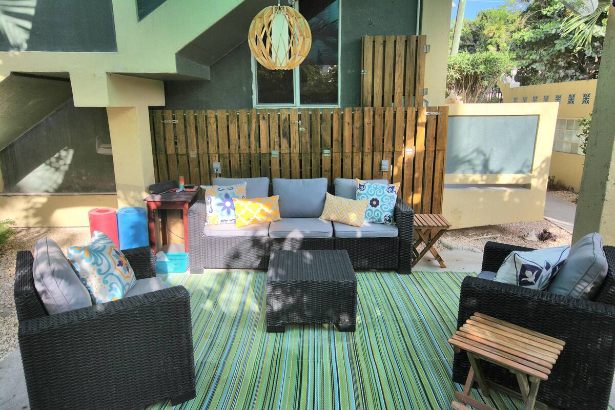 An outdoor seating area with wicker furniture, a striped rug, and a wooden fence.