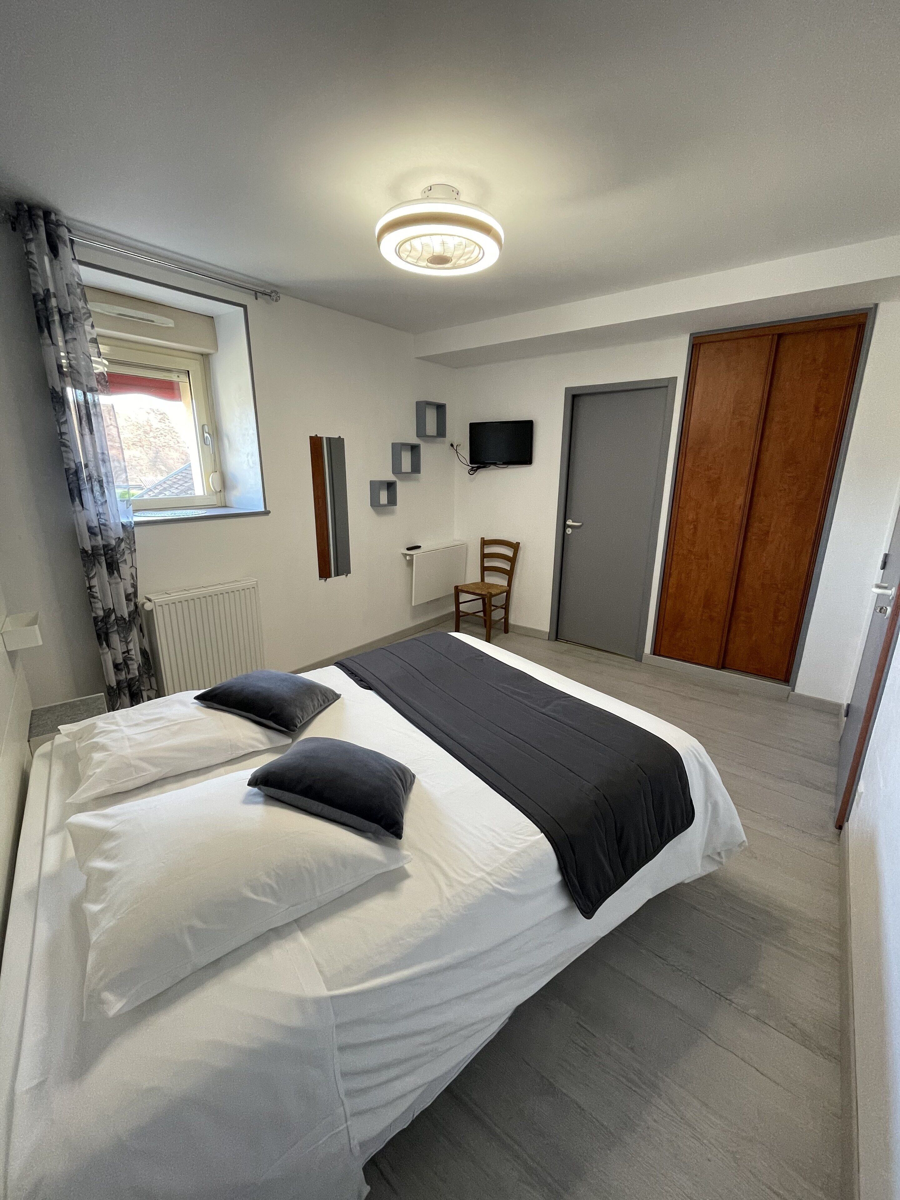 A bedroom with a bed, a window with curtains, a radiator, a television on the wall, and a door.