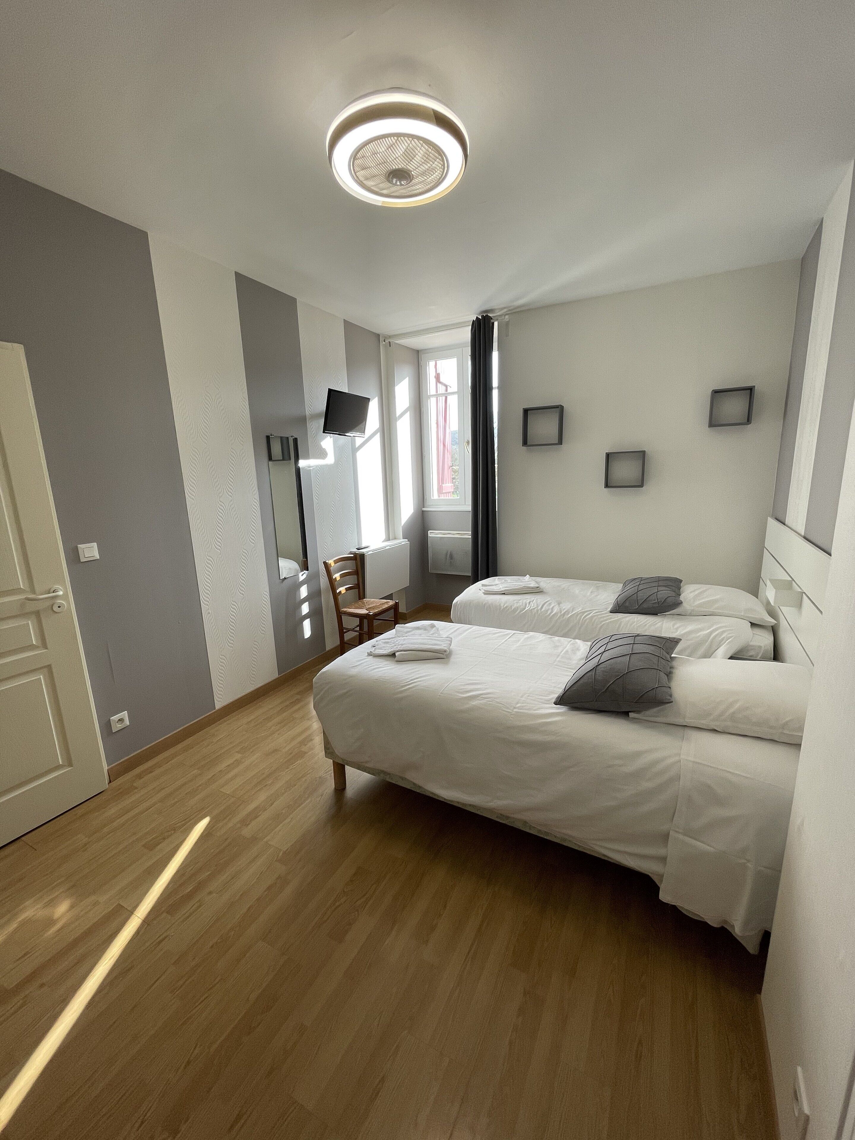 Een moderne hotelkamer met twee bedden, een flatscreen-televisie, een houten vloer en een plafondlamp.
