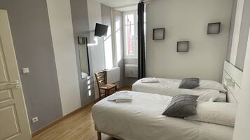 Een moderne hotelkamer met twee bedden, een flatscreen-televisie, een houten vloer en een plafondlamp.
