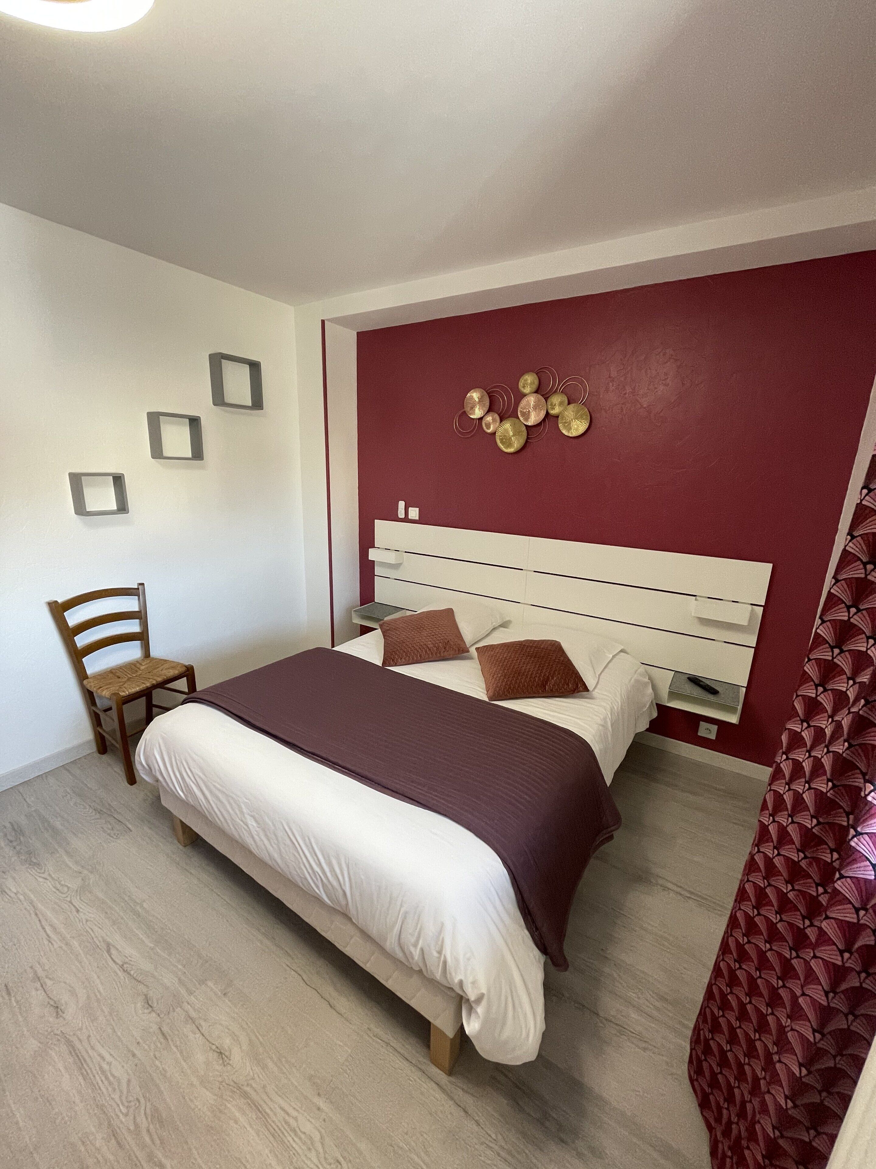 A bedroom with a bed, a chair, a bedside table, and a wall decoration.