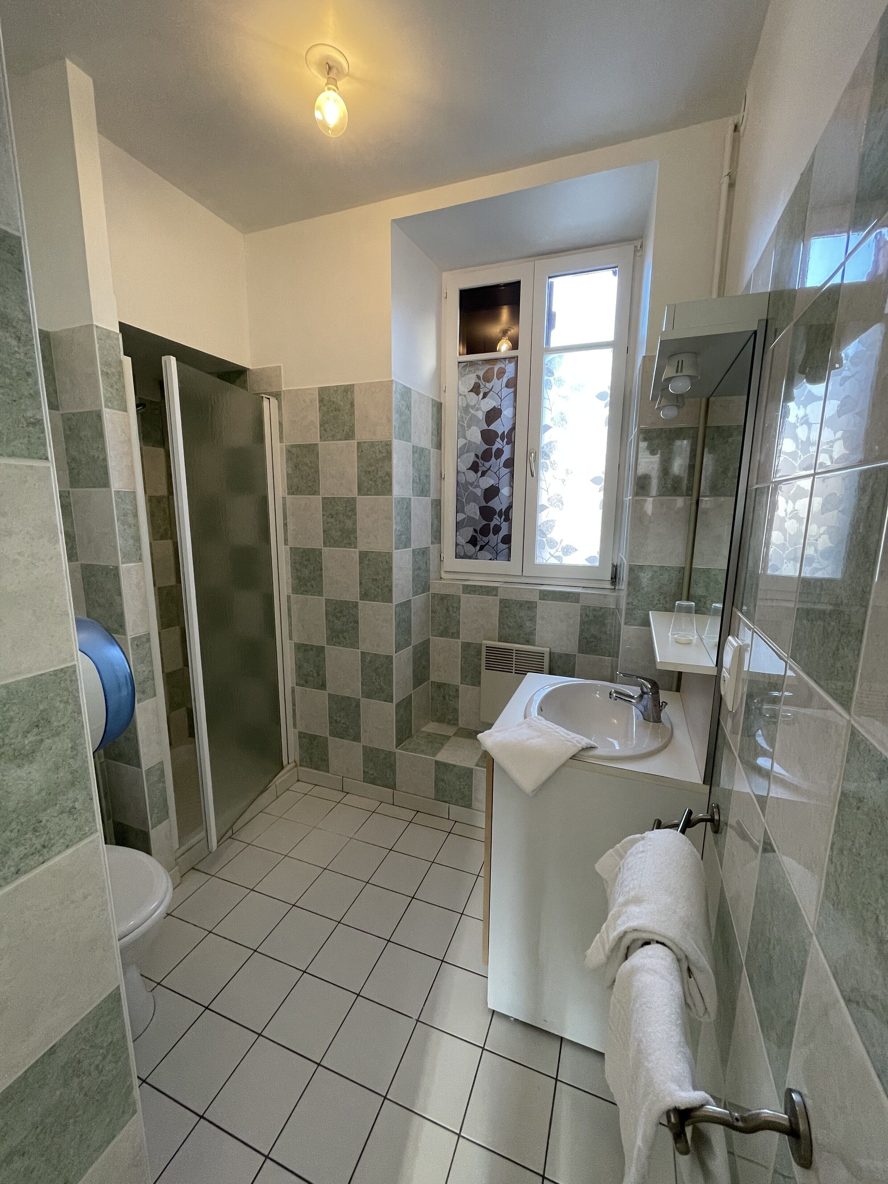 A bathroom with a shower, toilet, sink, and a window with a view.