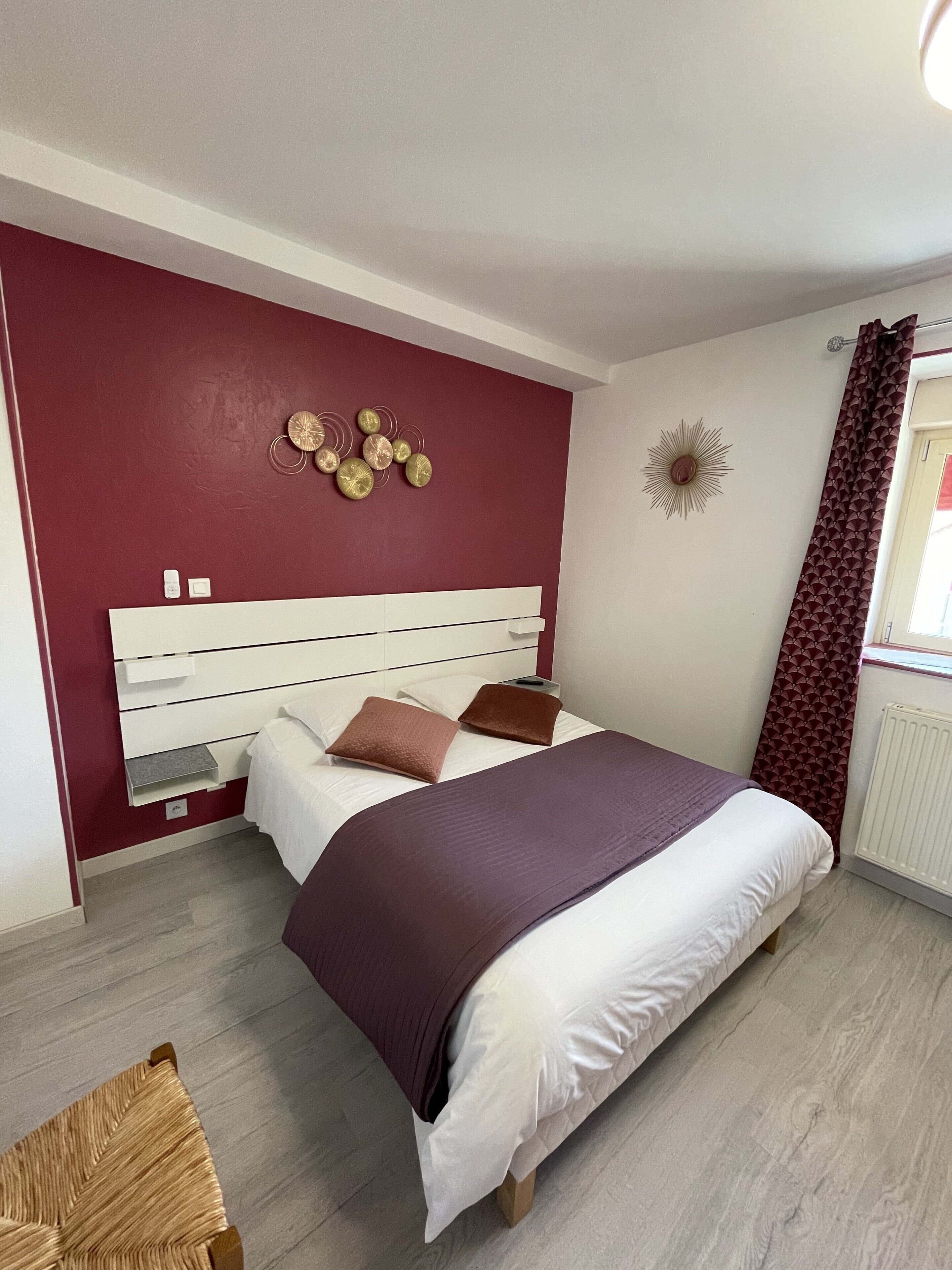 A bedroom with a bed, a headboard, a wall clock, and a window with curtains.