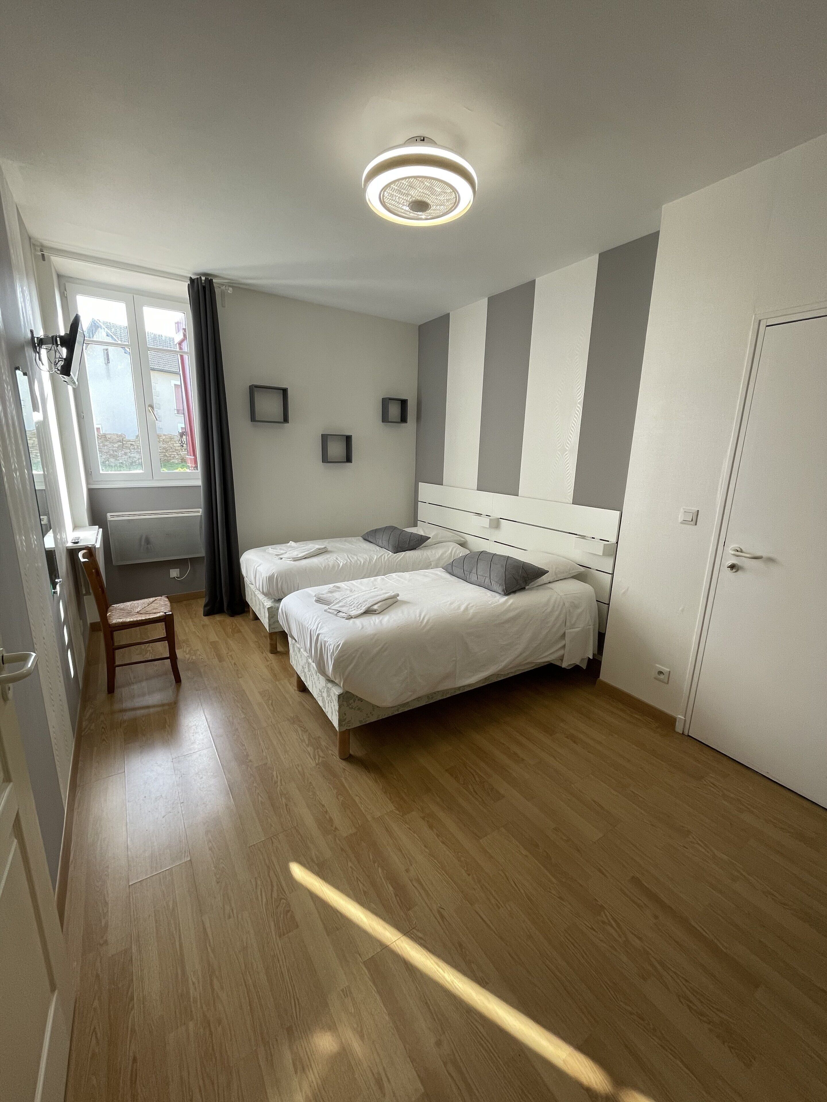 A modern hotel room with two beds, a wooden floor, a ceiling light, and a window with curtains.