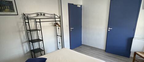 A bedroom with a bed, two pillows, a metal rack, two doors, and a ceiling light.