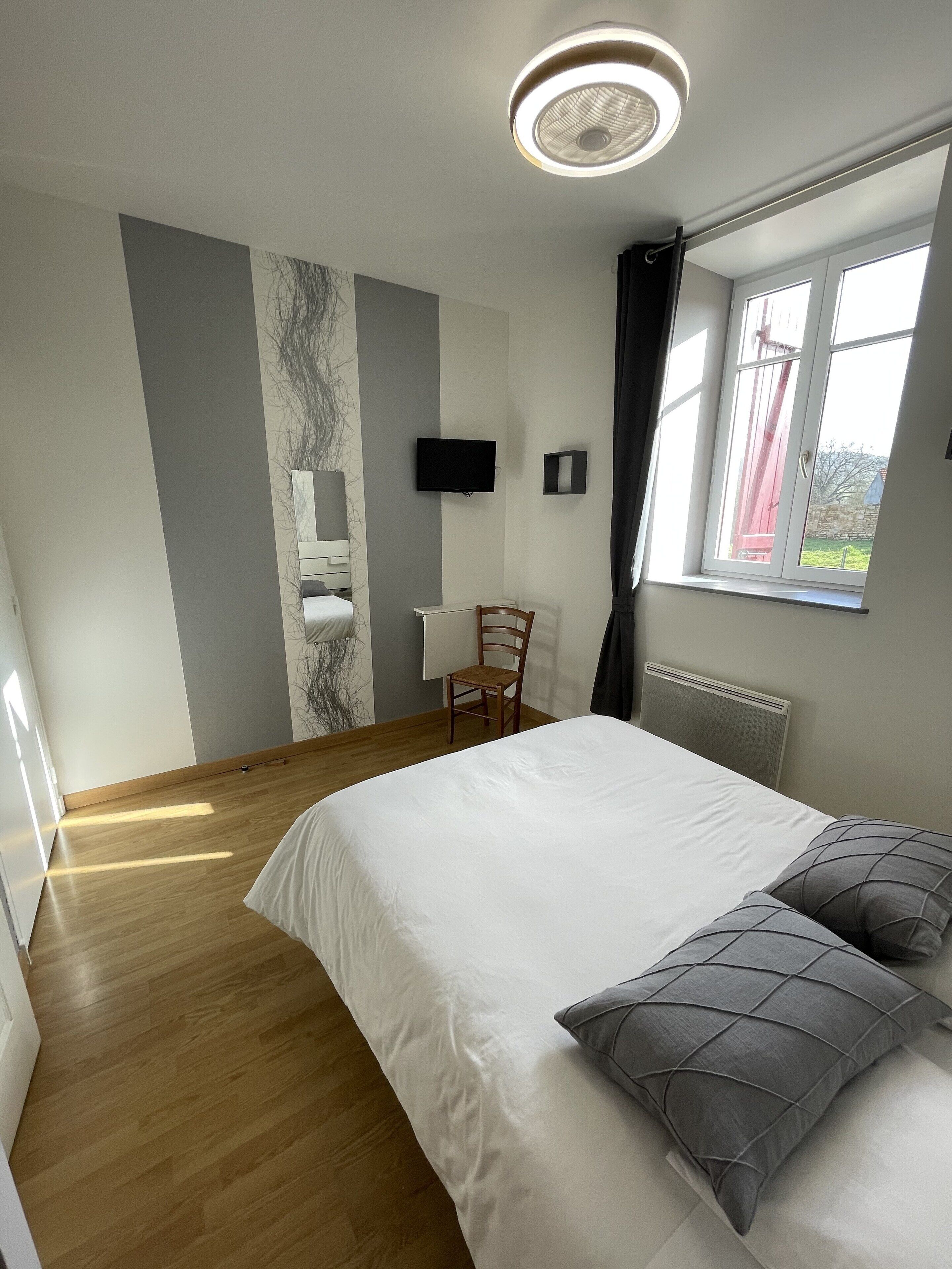 A modern bedroom with a large bed, a chair, a TV, and a window with a view.