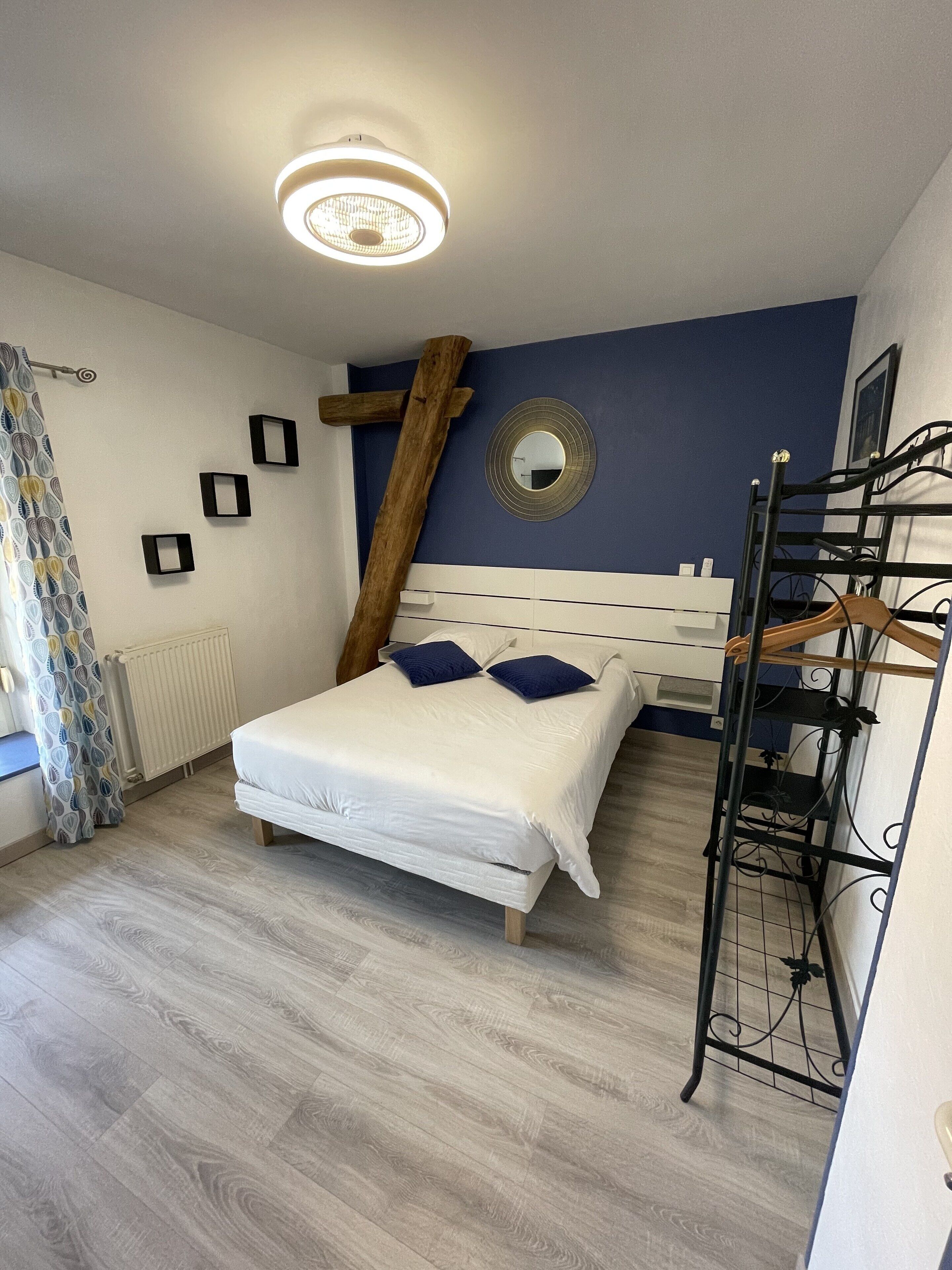 Ein Schlafzimmer mit Bett, Heizkörper, einer Holzlade, einem Spiegel und einer Deckenleuchte.