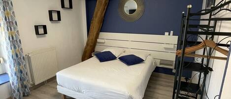 A bedroom with a bed, a radiator, a wooden ladder, a mirror, and a ceiling light fixture.