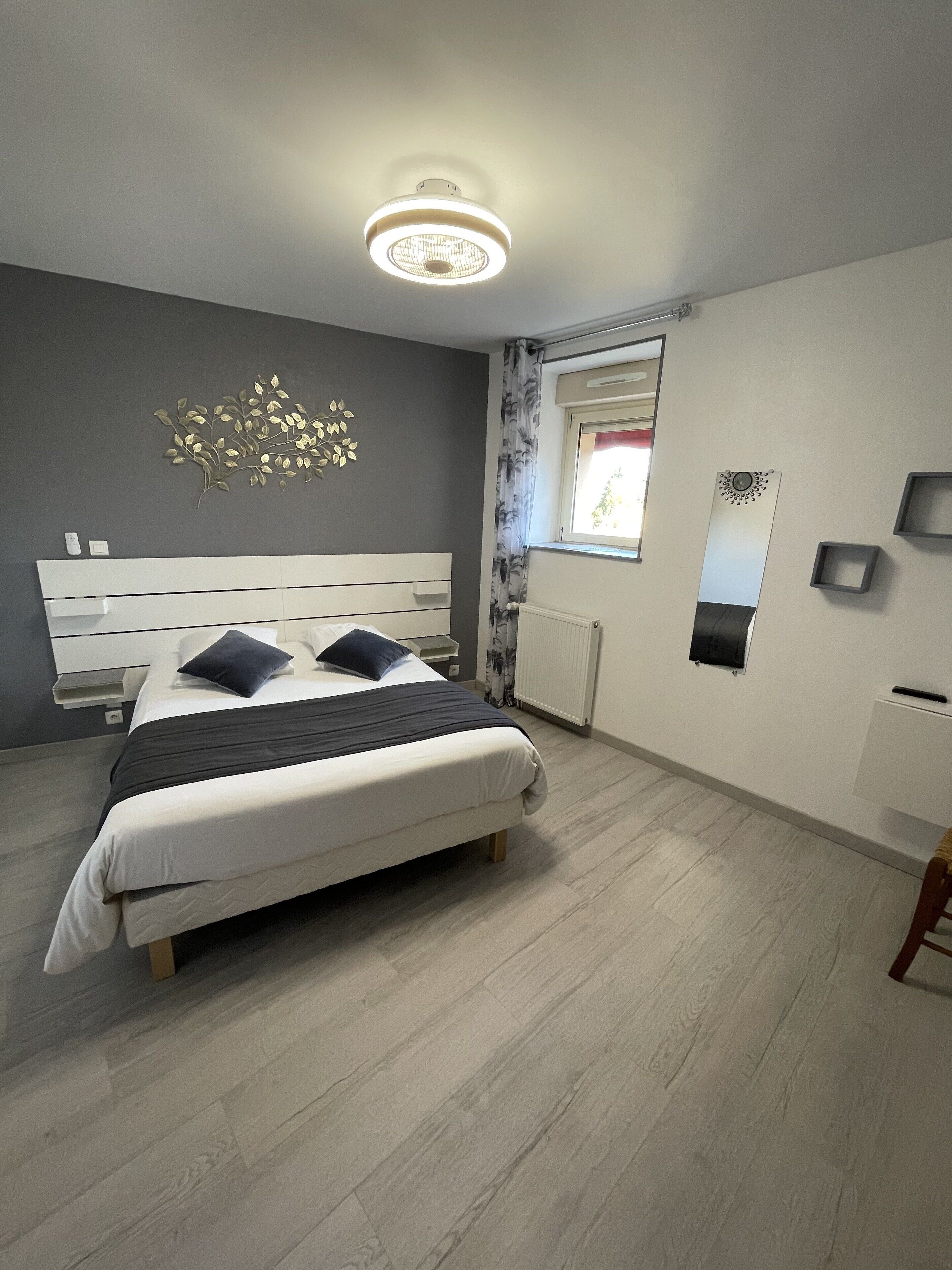 A modern bedroom with a bed, a ceiling light, a window with curtains, and a wall-mounted mirror.