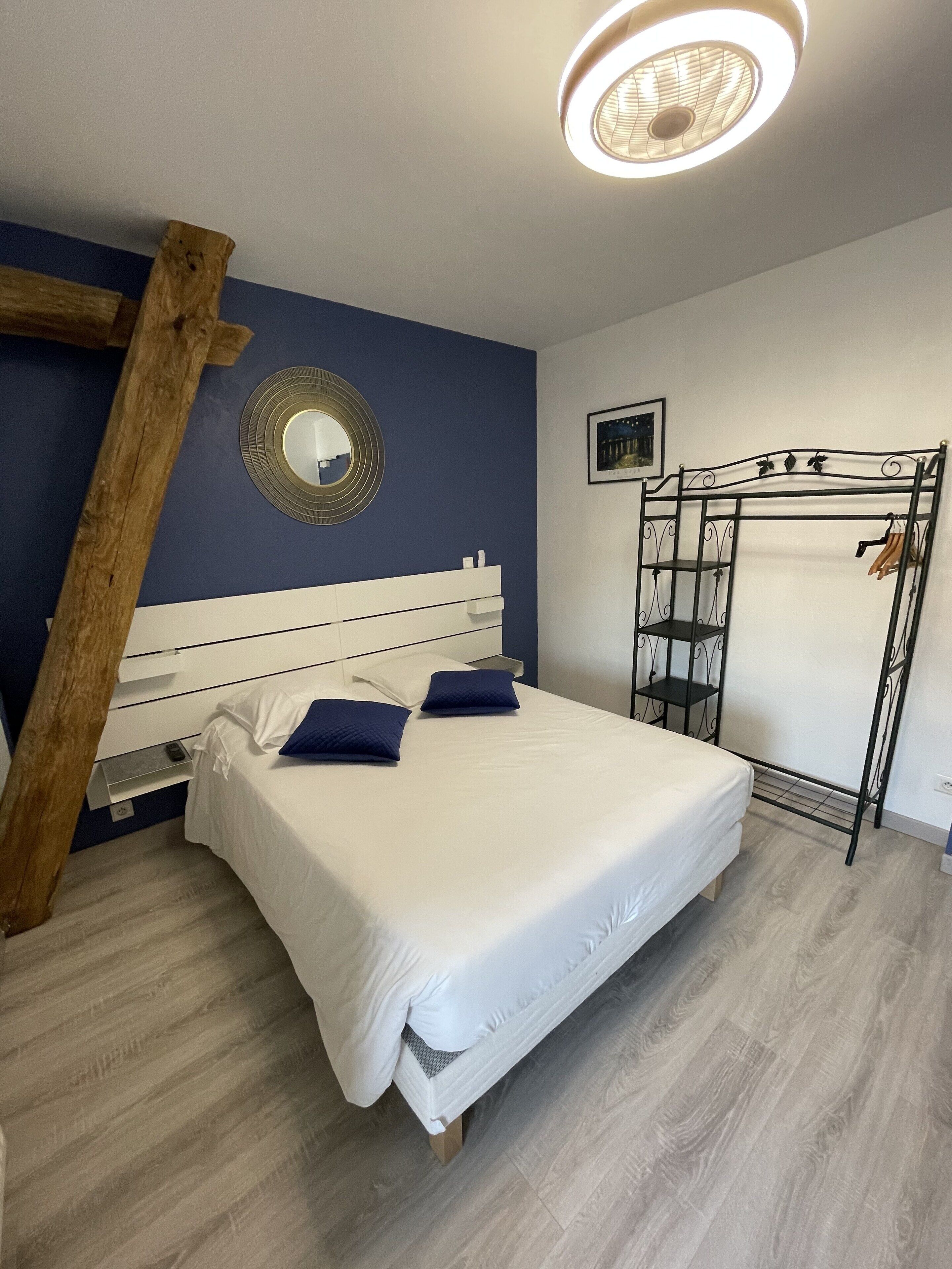 A bedroom with a bed, a wooden ladder, a mirror, and a metal rack.