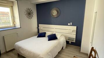 Un dormitorio con cama, una silla, una ventana y un aplique de pared.