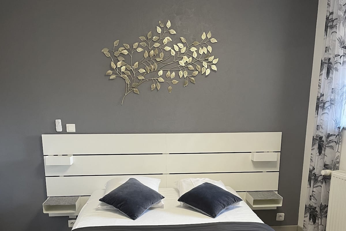 A modern bedroom with a bed, two pillows, a wall-mounted light, and a decorative leaf design.