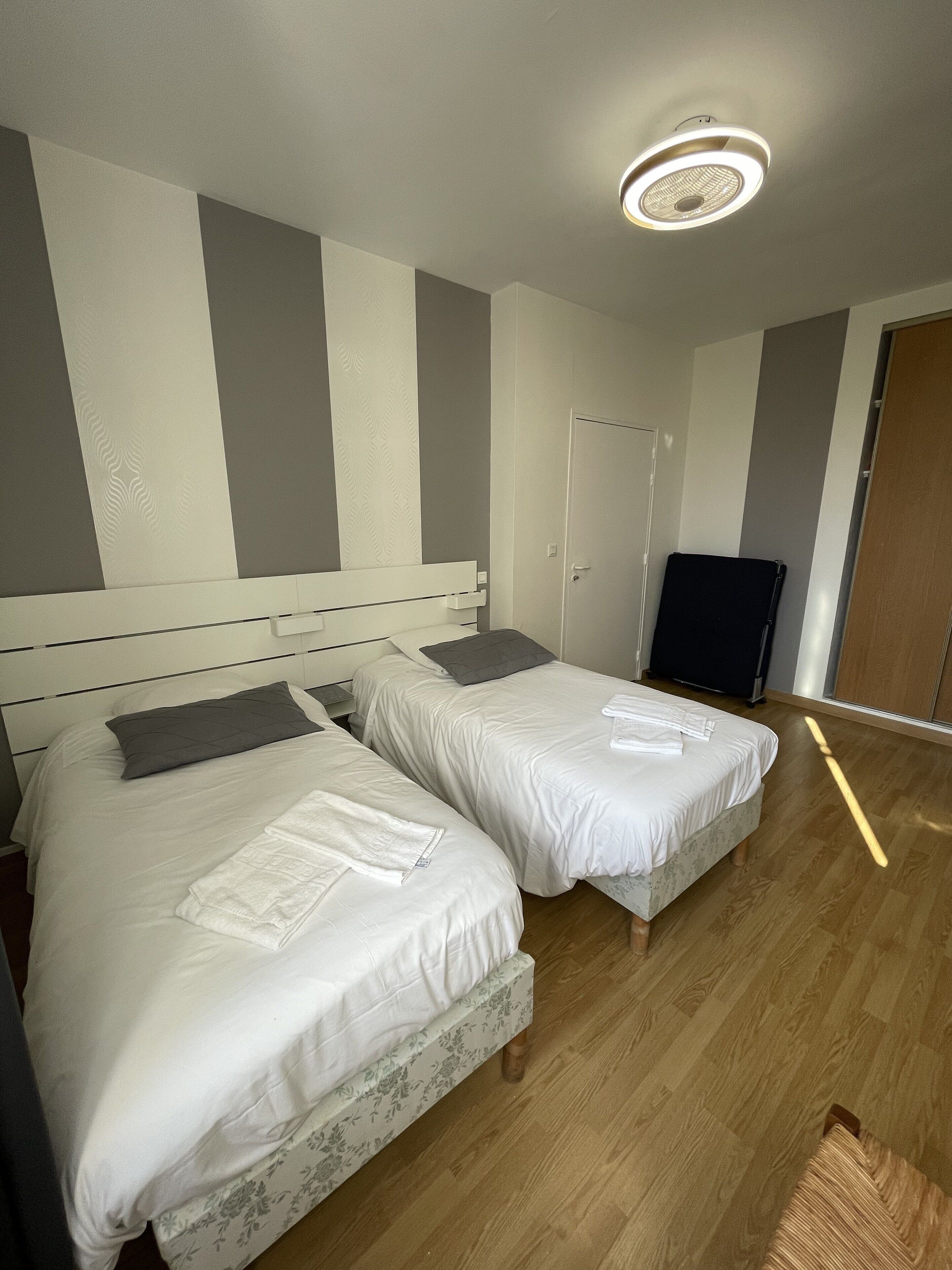 A hotel room with two beds, a wooden floor, and a ceiling light fixture.