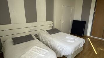 A hotel room with two beds, a wooden floor, and a ceiling light fixture.