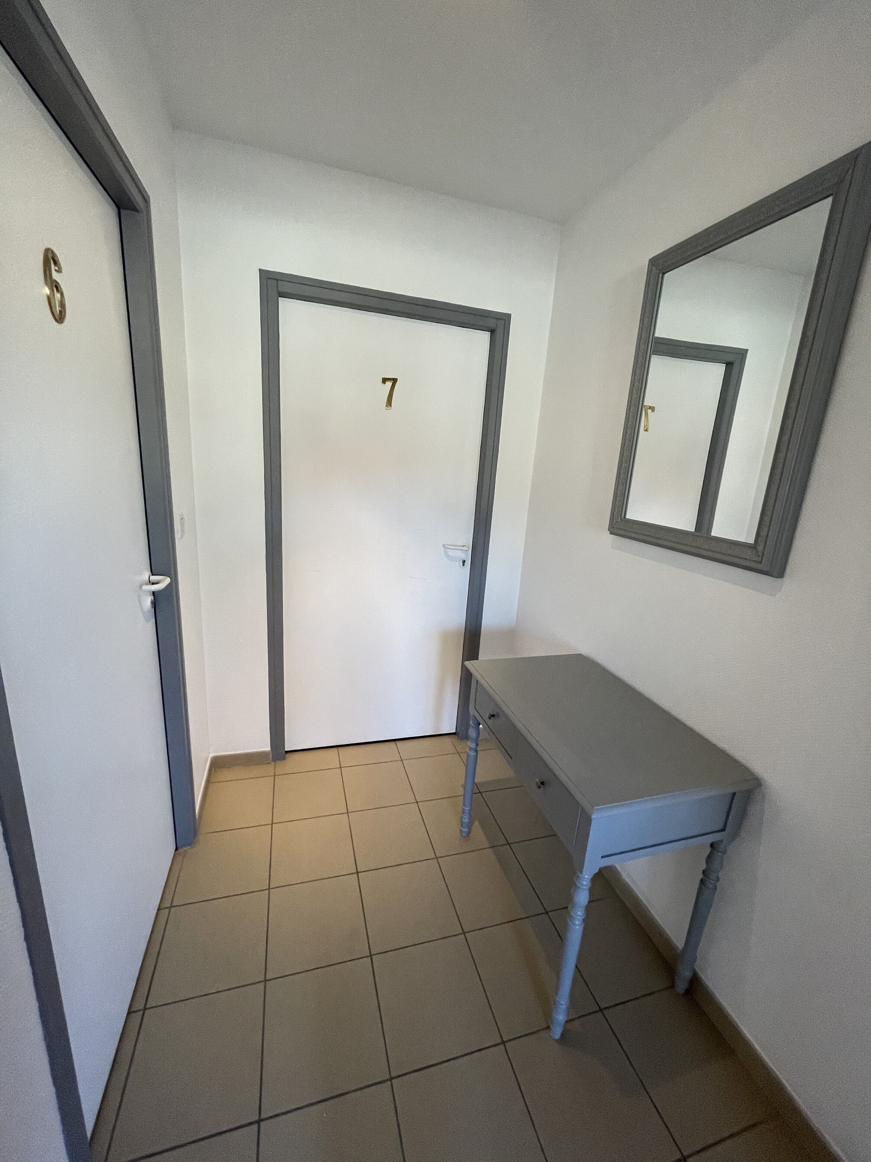 Un couloir avec une porte portant le numéro « 7 », un banc et un miroir accroché au mur.