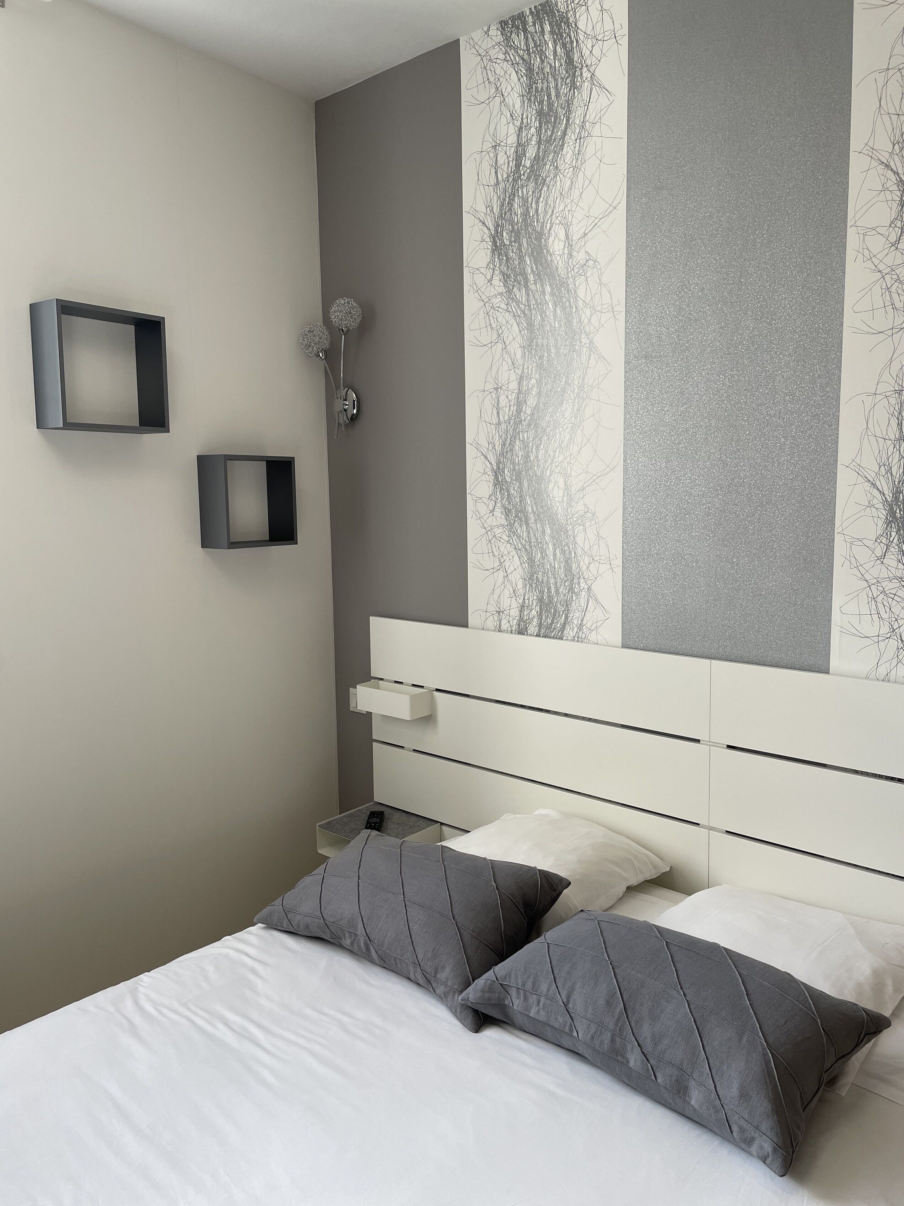 Un dormitorio moderno con cama, dos mesitas de noche, una mesita auxiliar y una lámpara fijada a la pared.