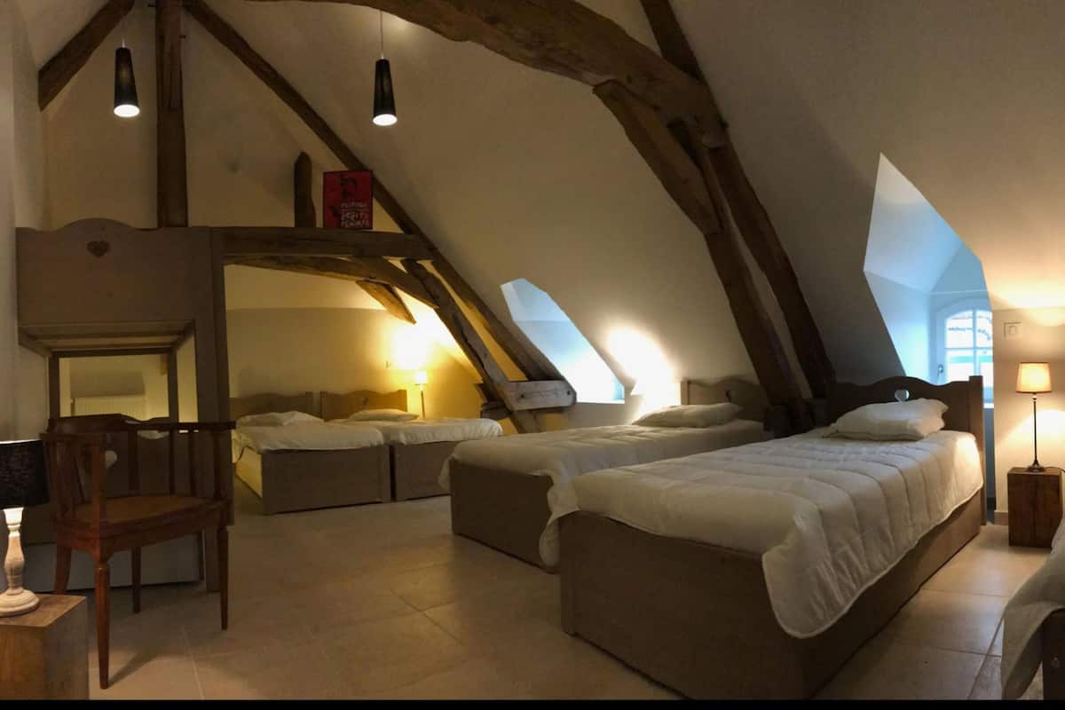 A cozy attic bedroom with two beds, a wooden chair, and a small table.
