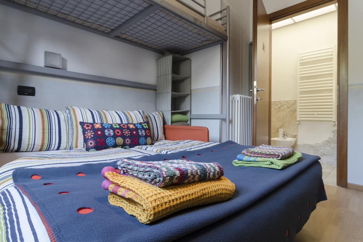 Een slaapkamer met een stapelbed, een nachtkastje, een radiator en een badkamer die door een open deur zichtbaar is.