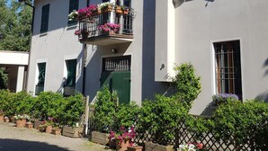 Un bâtiment à deux étages doté d’un balcon orné de fleurs, d’une cour pavée et d’une clôture.